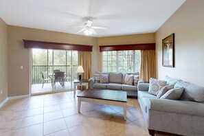 A spacious living room with a ceiling fan, a sofa, a coffee table, and a dining area with chairs and a lamp. - Inviting 4th-floor condo with Balcony, Shuttle & Resort Amenities (Orlando)