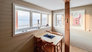 Ein gemütlicher Essbereich mit Tisch und Stühlen, große Fenster mit Blick auf das Meer und die Berge sowie ein Holzinterieur.