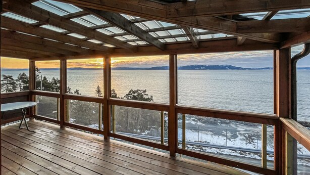Eine Holzterrasse mit großen Fenstern mit Blick auf ein Gewässer und eine verschneite Landschaft.