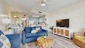 Una sala de estar moderna con un sofá azul, una mesa de centro redonda de madera y un televisor sobre un mueble blanco.