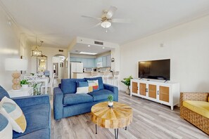 A modern living room with a blue sofa, a round wooden coffee table, and a television on a white cabinet. - Wonderful lakefront condo near Disney with view, kitchen, gym, pool & hot tub (Orlando)