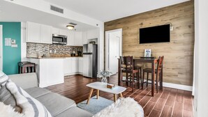 Eine moderne Küche mit weißen Schränken, einer eingebauten Mikrowelle und einem Kühlschrank. Es gibt einen Essbereich mit einem Holztisch und Stühlen.