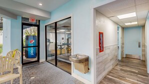 A hotel entrance with a Pepsi refrigerator, a water dispenser, and a seating area with plastic chairs. - Spacious Condo with a Kitchen, AC, Pools, Hot Tubs, Tennis, & Gym (Orlando)
