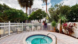 A hot tub surrounded by a white fence, with chairs and potted plants nearby. - Spacious Condo with a Kitchen, AC, Pools, Hot Tubs, Tennis, & Gym (Orlando)