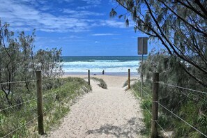 Un sentier de sable bordé d’une clôture en bois et d’un grillage, qui mène à l’océan.