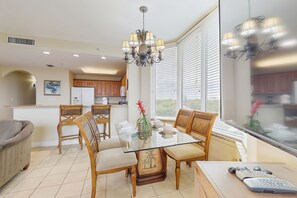 A dining area with a glass table, wooden chairs, and a chandelier. - Classy lakefront condo, w/ shared pool, hot tub, & fitness center - near Disney (Orlando)