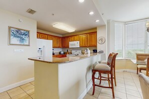 A modern kitchen with wooden cabinets, a central island with bar stools, a microwave, and a clock on the wall. - Classy lakefront condo, w/ shared pool, hot tub, & fitness center - near Disney (Orlando)