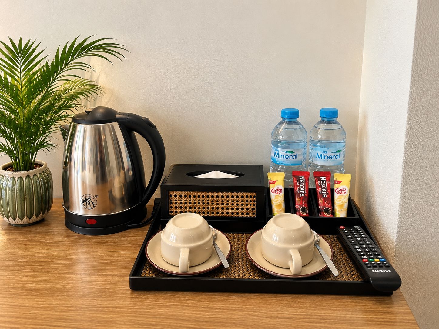 A tray with a coffee maker, two water bottles, a tissue box, and two cups on a wooden surface.