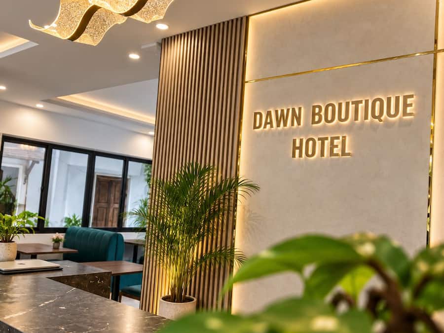 A reception area with a modern design, including a marble counter, a large potted plant, and a wall-mounted sign that reads 'DAWN BOUTIQUE HOTEL.'