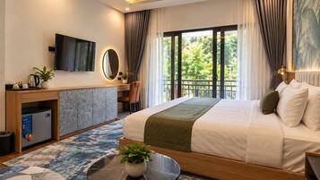 Habitación de hotel moderna con cama, escritorio, televisión y balcón con vista a zonas verdes.
