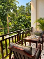 A balcony with a wooden railing, a table with a laptop, a chair with cushions, and a potted plant.