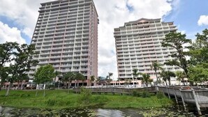 Two high-rise buildings with multiple balconies, surrounded by greenery and a body of water. - Lakefront condo with beautiful views, wifi, central AC, shared pool, & hot tub (Orlando)