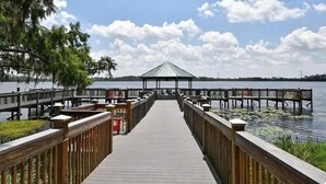 A wooden pier leading to a gazebo over water, surrounded by trees and docked boats. - Lakefront condo with beautiful views, wifi, central AC, shared pool, & hot tub (Orlando)