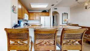 A kitchen with wooden cabinets, a central island with chairs, a microwave, and a refrigerator. - Lakefront condo with beautiful views, wifi, central AC, shared pool, & hot tub (Orlando)