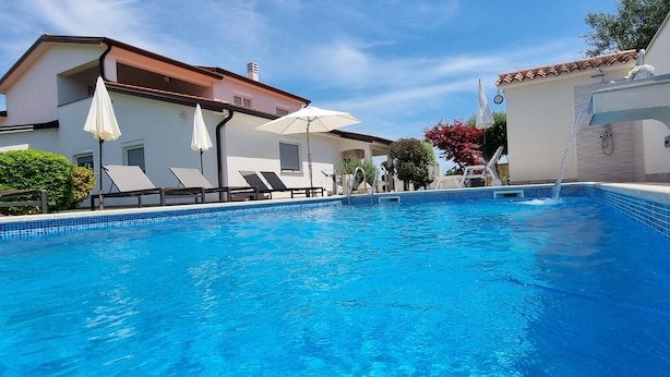 A swimming pool with lounge chairs and umbrellas, surrounded by buildings with a tiled roof and white walls. - Villa Kasandra Peace & elegance in Buje, Istria (Kaštel)