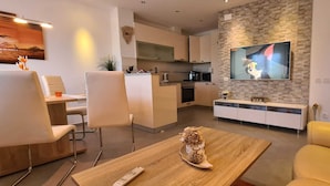 A modern living room with a wooden coffee table, a TV mounted on a brick wall, and a kitchen in the background. - Villa Kasandra Peace & elegance in Buje, Istria (Kaštel)