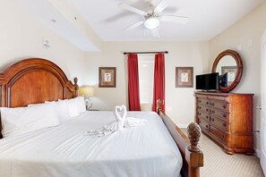 A hotel room with a large bed, a wooden dresser, a television, and a ceiling fan. - Charming lakefront condo with balcony, lake view, AC, Internet, pool & hot tub (Orlando)