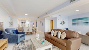 Un ampli saló amb un sofà marró, un butàc armchair blau i una taula de centre de fusta. Al fons, hi ha una zona de menjador amb una taula i cadires.