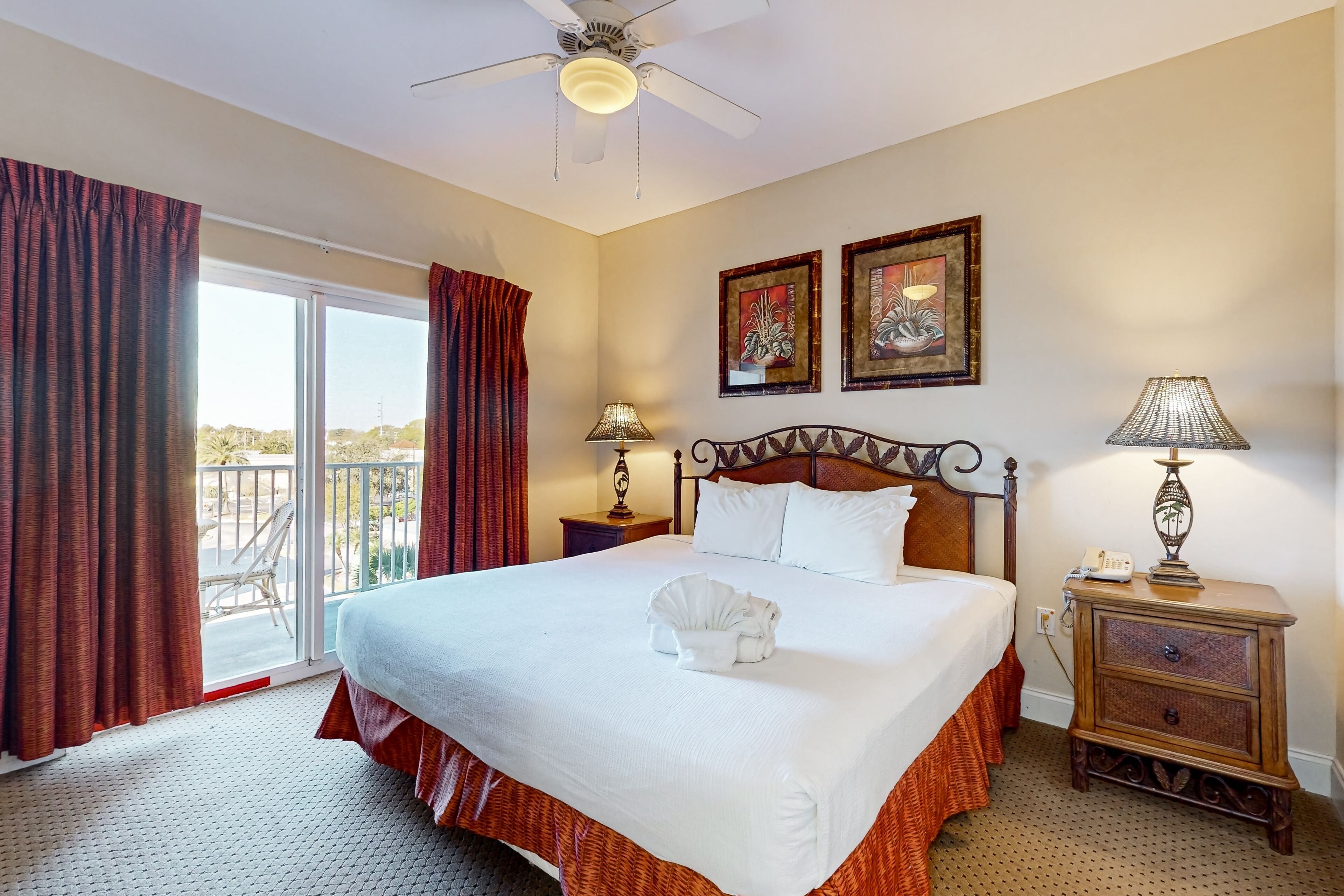 Une chambre d’hôtel avec un grand lit, un ventilateur de plafond, deux lampes de chevet, une table de chevet et une vue sur l’extérieur grâce à une porte coulissante.