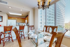 A dining area with a glass table, wooden chairs, and a view of the outside through large windows. - Spacious lakefront condo with views, AC, gym, pool & hot tub near attractions (Orlando)