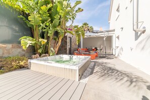 Een jacuzzi in een achtertuin met een stenen muur, een houten terras en een patio.