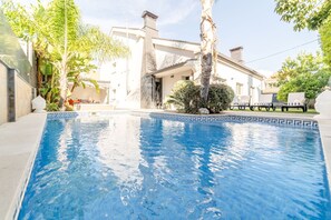 A swimming pool with a geometric tile border, surrounded by lush greenery and a modern house with a visible chimney. - Villa Solmaris | Costa da Caparica | Private Pool - Jacuzzi | Near Beach (Lisbon)