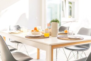 A breakfast table with a white tablecloth, woven placemats, a bowl of fruit, a glass of orange juice, and a potted plant. - Villa Solmaris | Costa da Caparica | Private Pool - Jacuzzi | Near Beach (Lisbon)