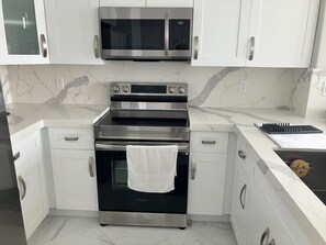 Eine Küche mit weißen Schränken, einem Edelstahlbackofen, einer Mikrowelle und einer Marmor-Spritzschutzwand.