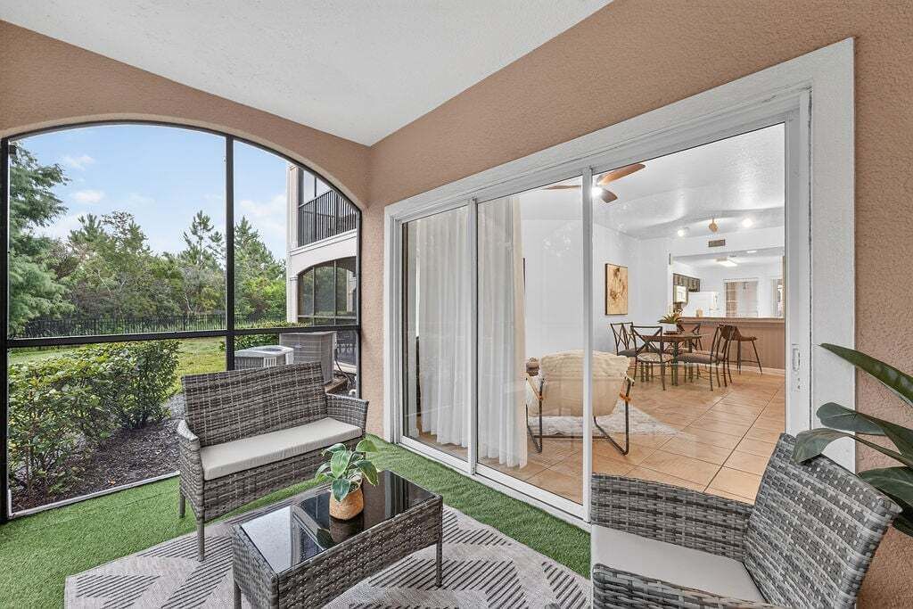 Ein Balkon mit Korbmöbeln, einem Glastisch und Blick auf den Garten.