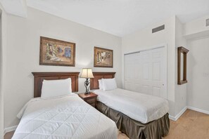 Ein Hotelzimmer mit zwei Betten, einem Nachttisch mit Lampe, einer Tür und zwei gerahmten Bildern an der Wand.