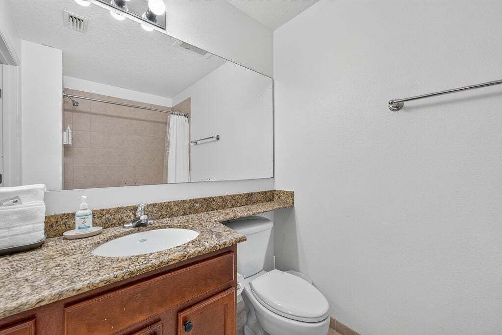 A bathroom with a granite countertop sink, a mirror, a towel rack, and a toilet.