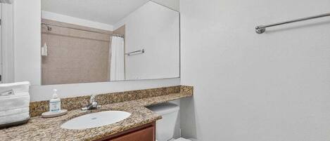 A bathroom with a granite countertop sink, a mirror, a towel rack, and a toilet.