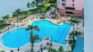 Una amplia piscina curvada rodeada de sillones de descanso y sombrillas, con un edificio al fondo.