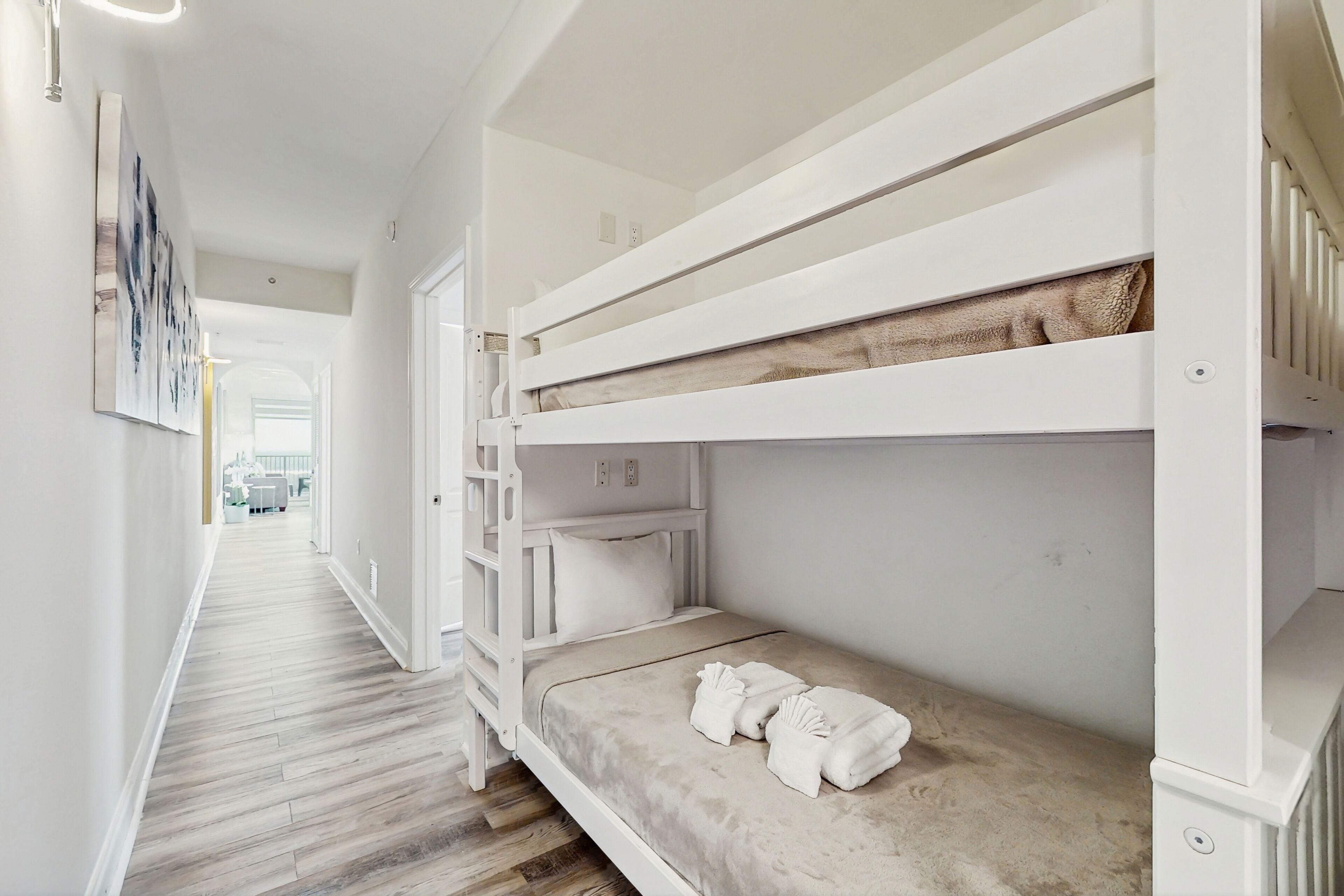 Une chambre avec un lit superposé, un plancher en bois, un mur blanc et un tableau encadré.