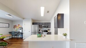 Cozinha moderna com ilha central, eletrodomésticos de aço inoxidável e área de jantar com mesa e cadeiras de madeira.