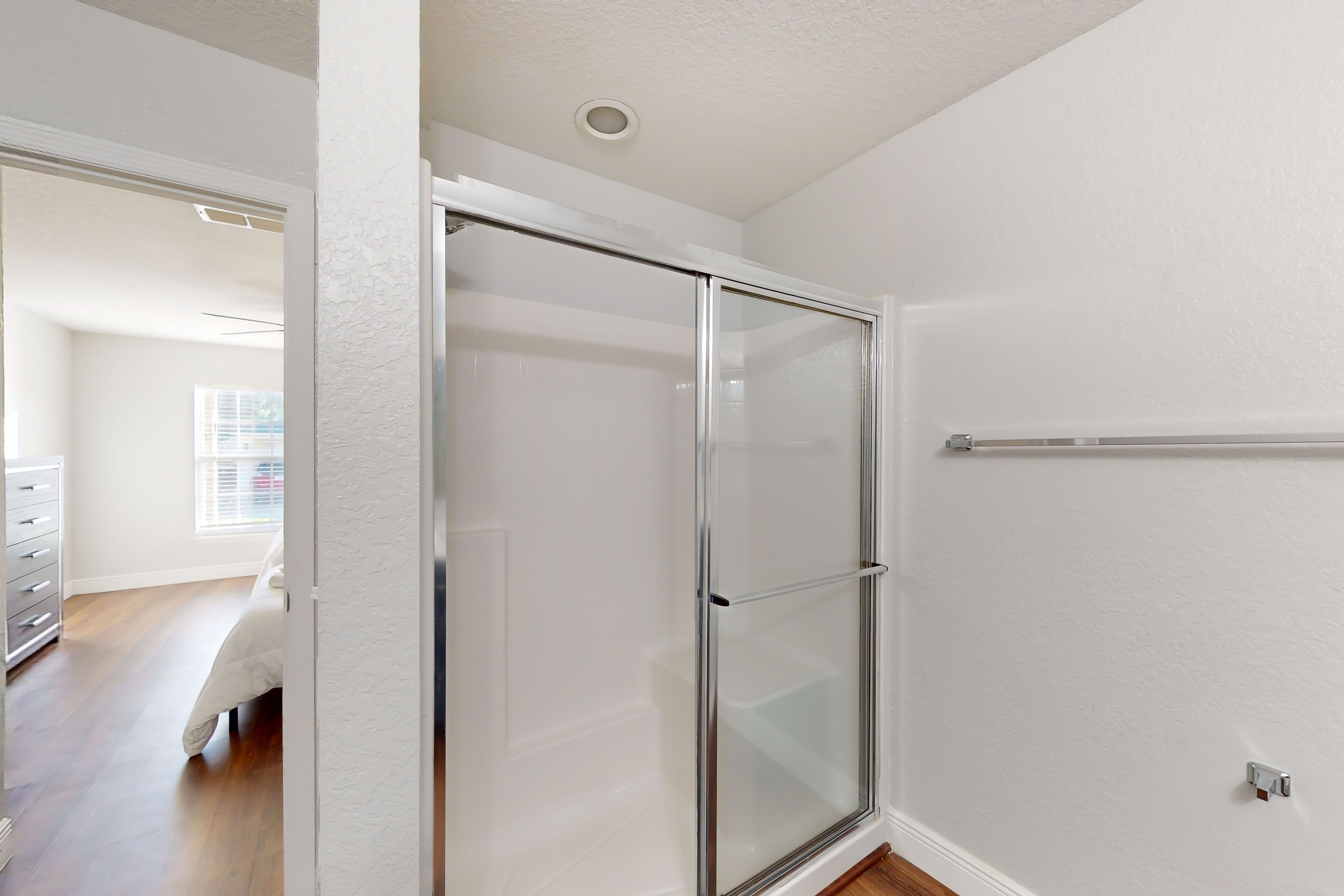 A modern bathroom with a glass shower enclosure, white walls, and a wooden floor.