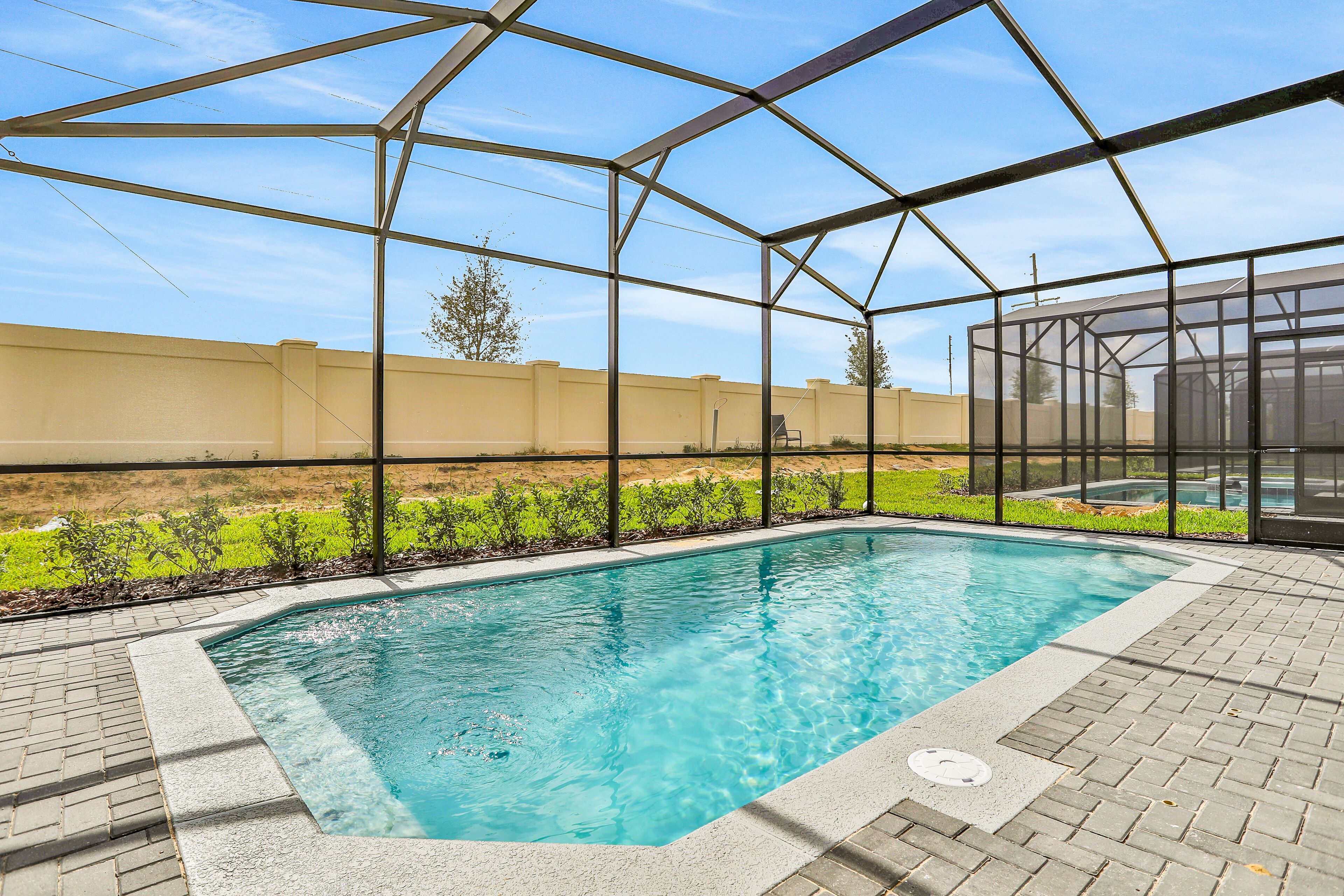Une piscine à l’eau d’un bleu limpide, entourée d’une terrasse en briques et protégée par une structure en verre.