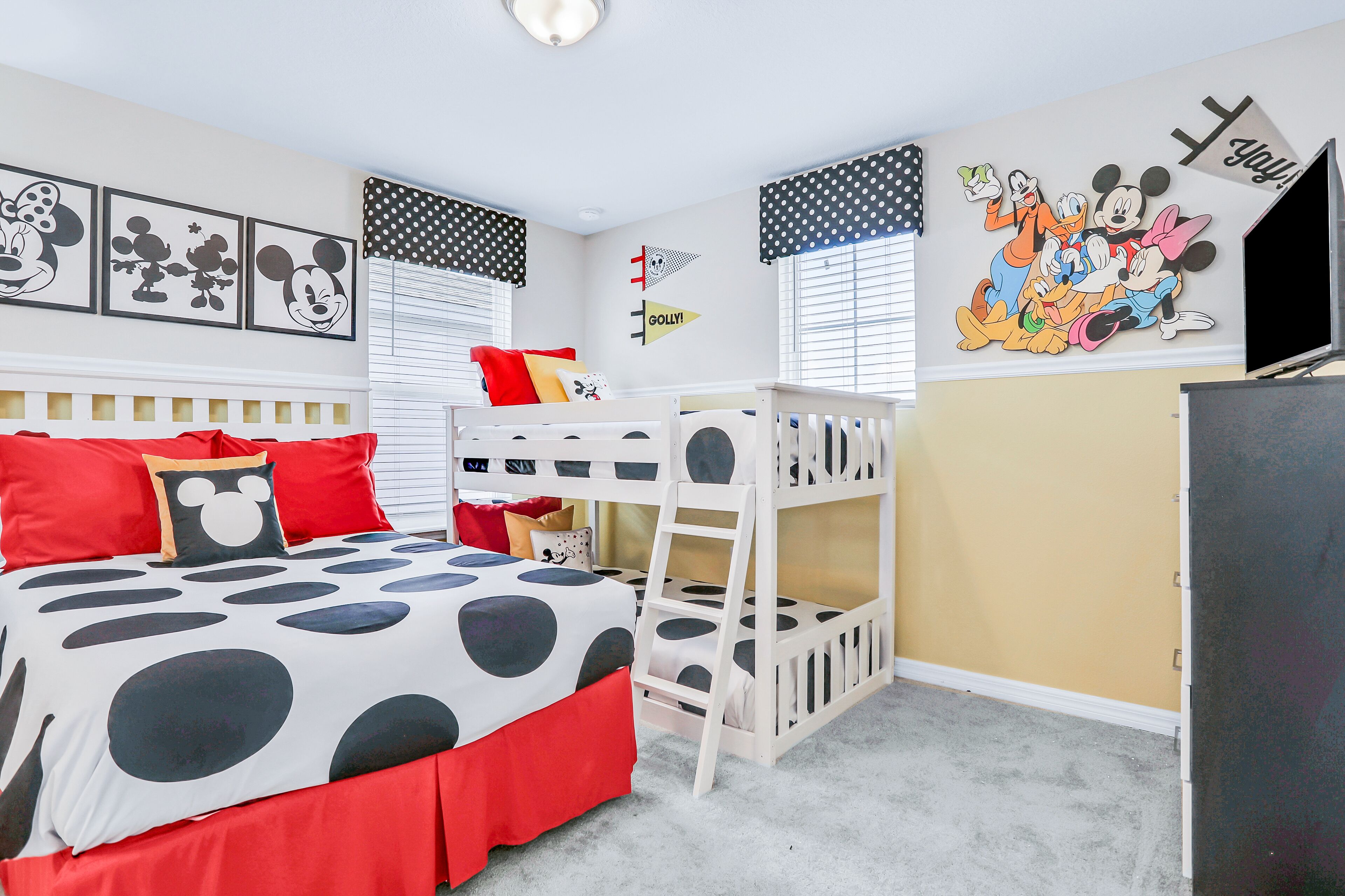 A child's bedroom with a bunk bed, polka dot bedding, Mickey Mouse pillows, and Disney-themed wall art.