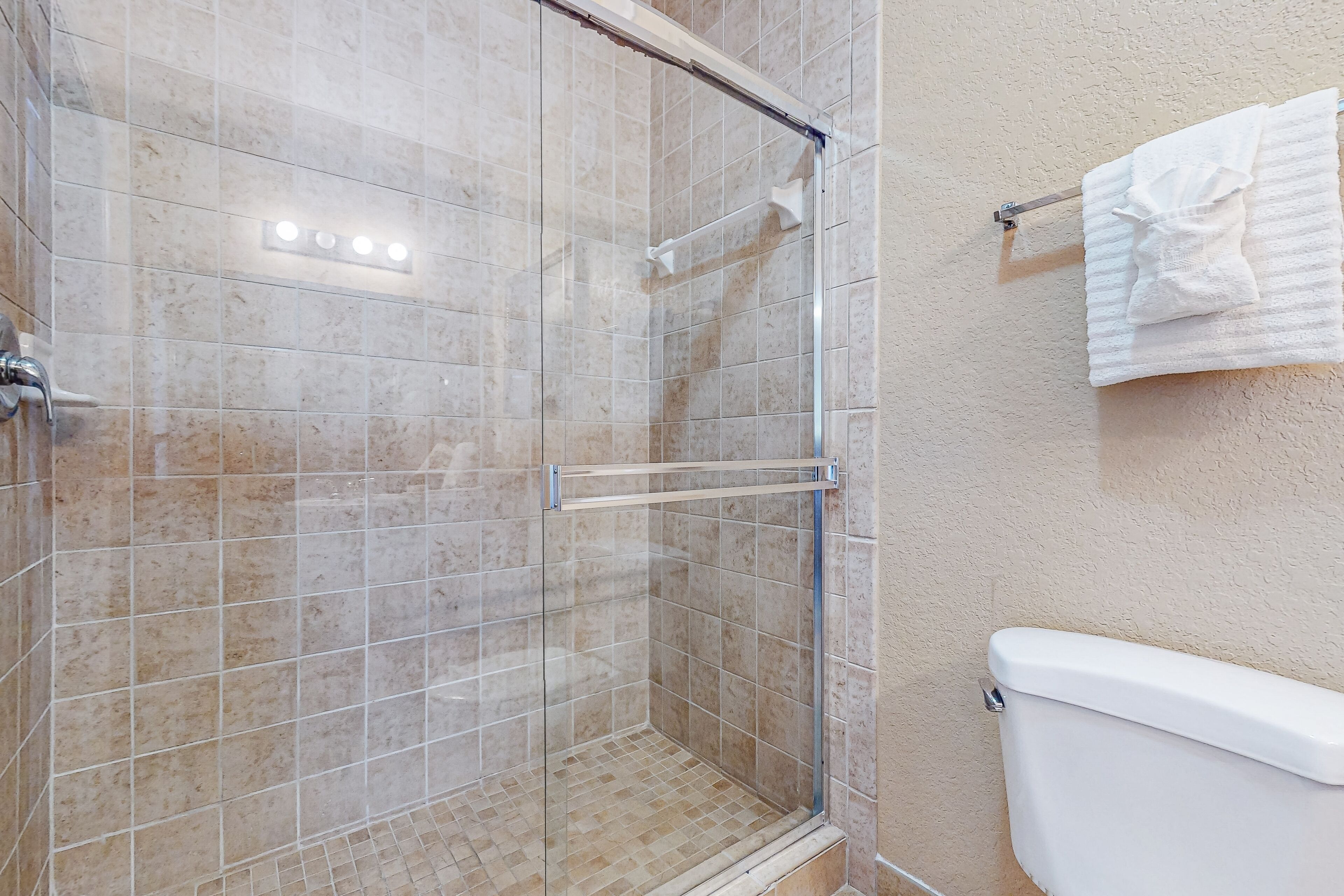 A shower with a glass door, tiled walls, and a white toilet.