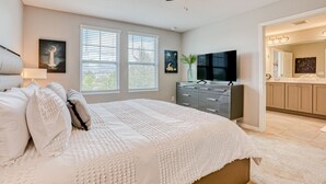 A bedroom with a large bed, a ceiling fan, a dresser, a TV, and a bathroom visible through an open door. - Spacious townhome with heated pool, WiFi, & central A/C - near theme parks (Davenport)