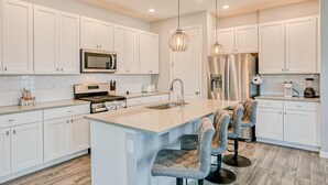 A modern kitchen with white cabinets, stainless steel appliances, and a central island with bar stools. - Spacious townhome with heated pool, WiFi, & central A/C - near theme parks (Davenport)