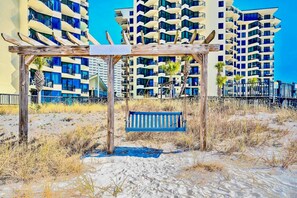 Ein Strand mit einer Holzpergola und einer Bank, umgeben von trockenem Gras und Sand.