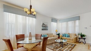 Uma sala de estar com uma mesa de jantar de vidro, dois sofás, uma mesa de centro e um tapete estampado.