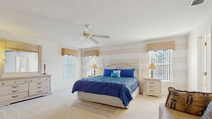 Quarto com cama, penteadeira, mesas de cabeceira e ventilador de teto.