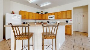 Uma cozinha com armários de madeira, uma geladeira branca, um micro-ondas e dois banquetas altas.