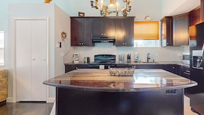 A modern kitchen with dark cabinets, a large island, a chandelier, and a hexagonal tile backsplash. - Riverfront home with internet, washer and dryer, and perfect for kayaking (Sebring)