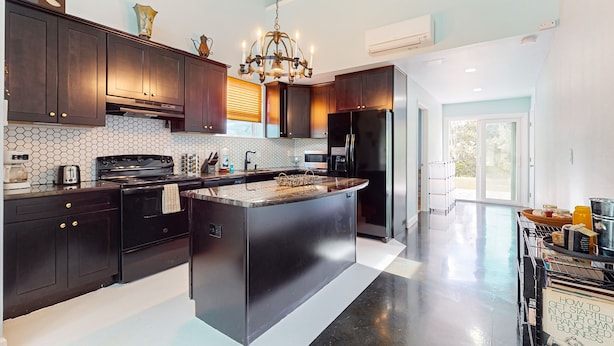 A modern kitchen with dark wood cabinets, a large island, stainless steel appliances, and a chandelier. - Riverfront home with internet, washer and dryer, and perfect for kayaking (Sebring)
