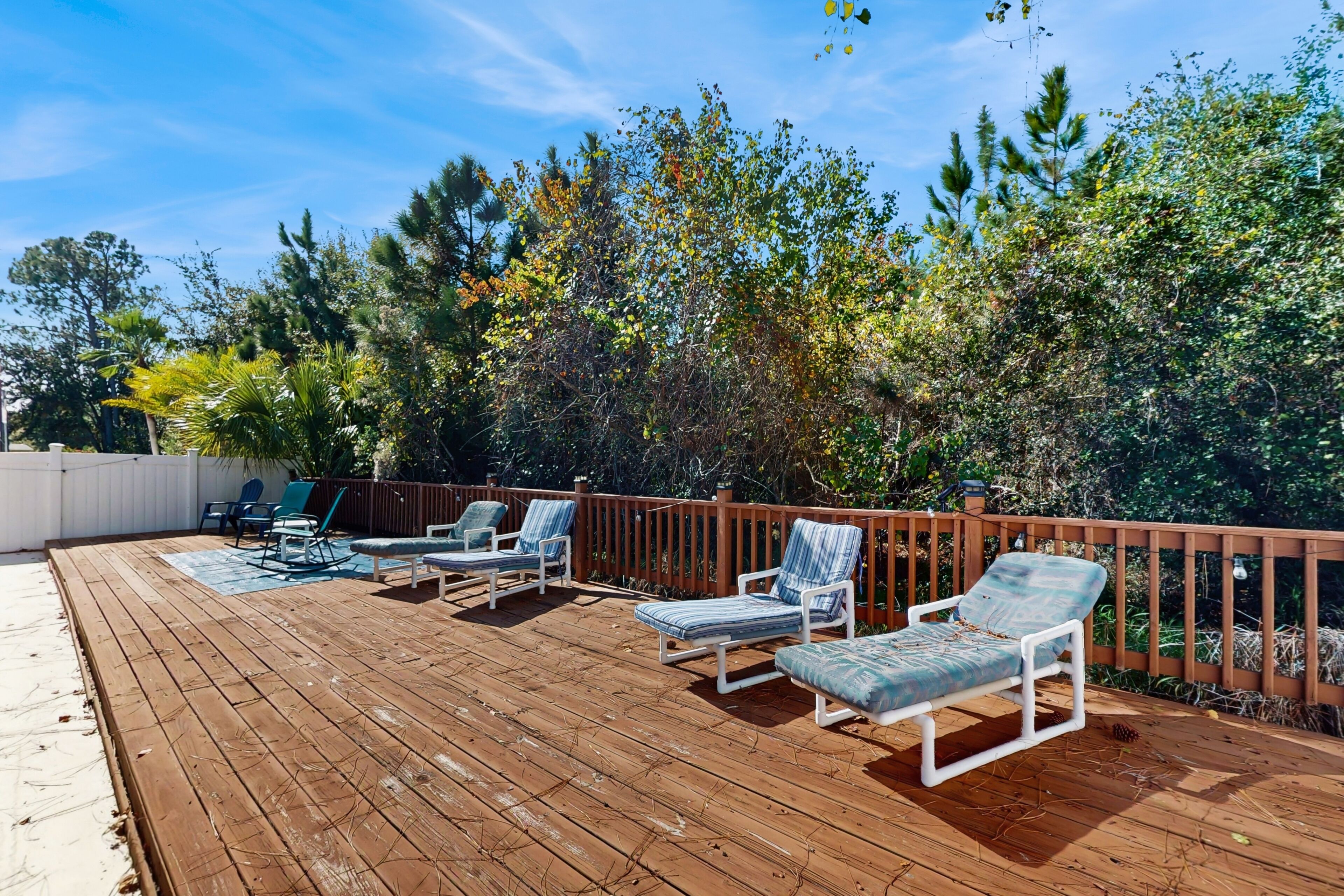 A wooden deck with lounge chairs and a white fence.