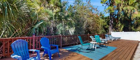 Une terrasse en bois avec des chaises Adirondack bleues et un tapis d’extérieur bleu.