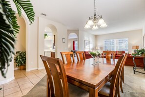 A spacious dining area with a wooden table and chairs, a chandelier, and a view of the living room in the background. - 5BR/3BA Davenport home with private pool (Davenport)